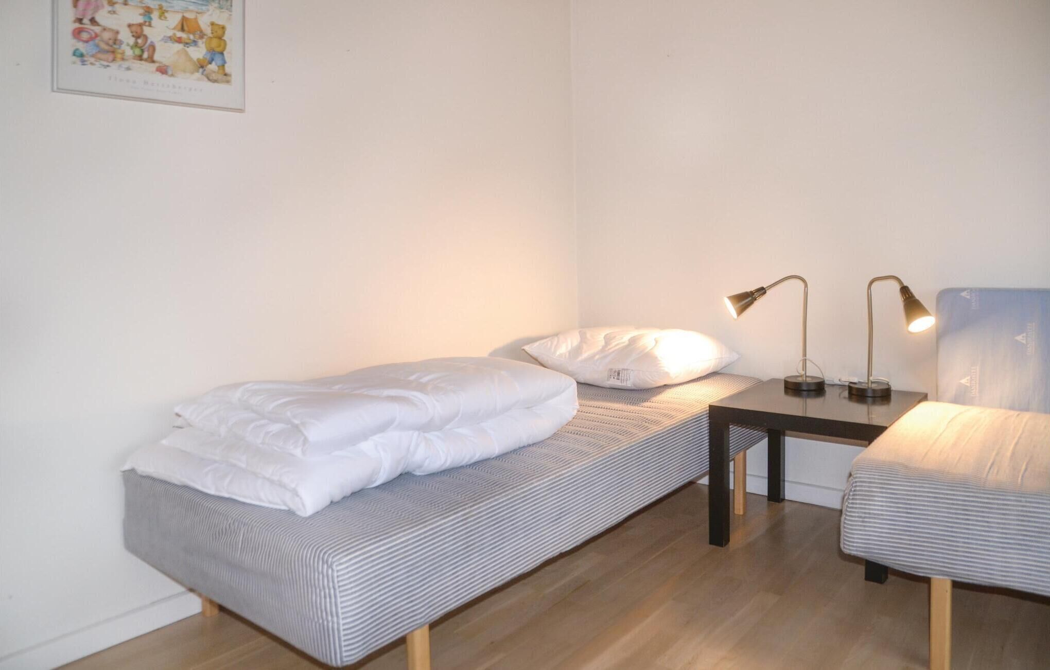 A small, neatly arranged bedroom with a single bed, a bedside table with two lamps, and a chair.