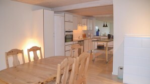 Un coin repas avec une table et des chaises en bois, une cuisine avec des meubles blancs et des appareils électroménagers, et un petit îlot central doté d’un évier et d’un plan de travail.