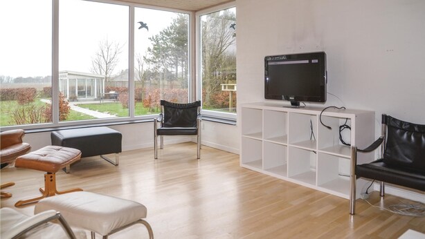 Un salon moderne doté de grandes fenêtres, d’un téléviseur à écran plat et de fauteuils en cuir.