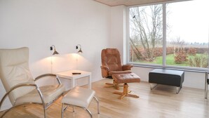Une chambre moderne dotée d’une grande fenêtre, d’un fauteuil inclinable en cuir, d’un fauteuil blanc et d’une petite table sur laquelle se trouve une télécommande.