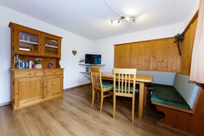 A wooden dining table with chairs, a television on a shelf, and a wooden cabinet with glass doors. - Apartment 1 - House Maringele (Nesselwängle)