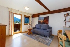 Ein Zimmer mit einer Couch, einem Holztisch, einem Bücherregal, einem Fenster mit Vorhängen und einem Bild an der Wand.