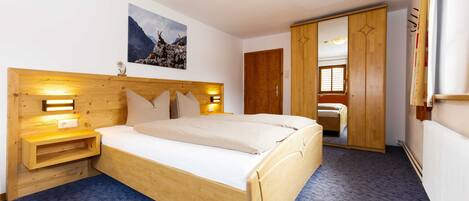 A bedroom with a wooden bed, bedside lamps, a nightstand, a wooden wardrobe, and a large mirror.