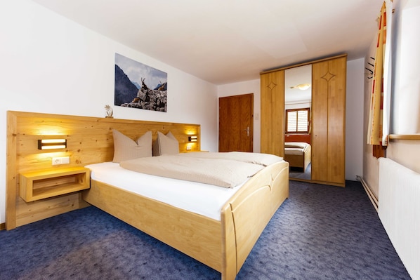 Un dormitorio con una cama de madera, lámparas de noche, una mesita de noche, un armario de madera y un espejo grande.
