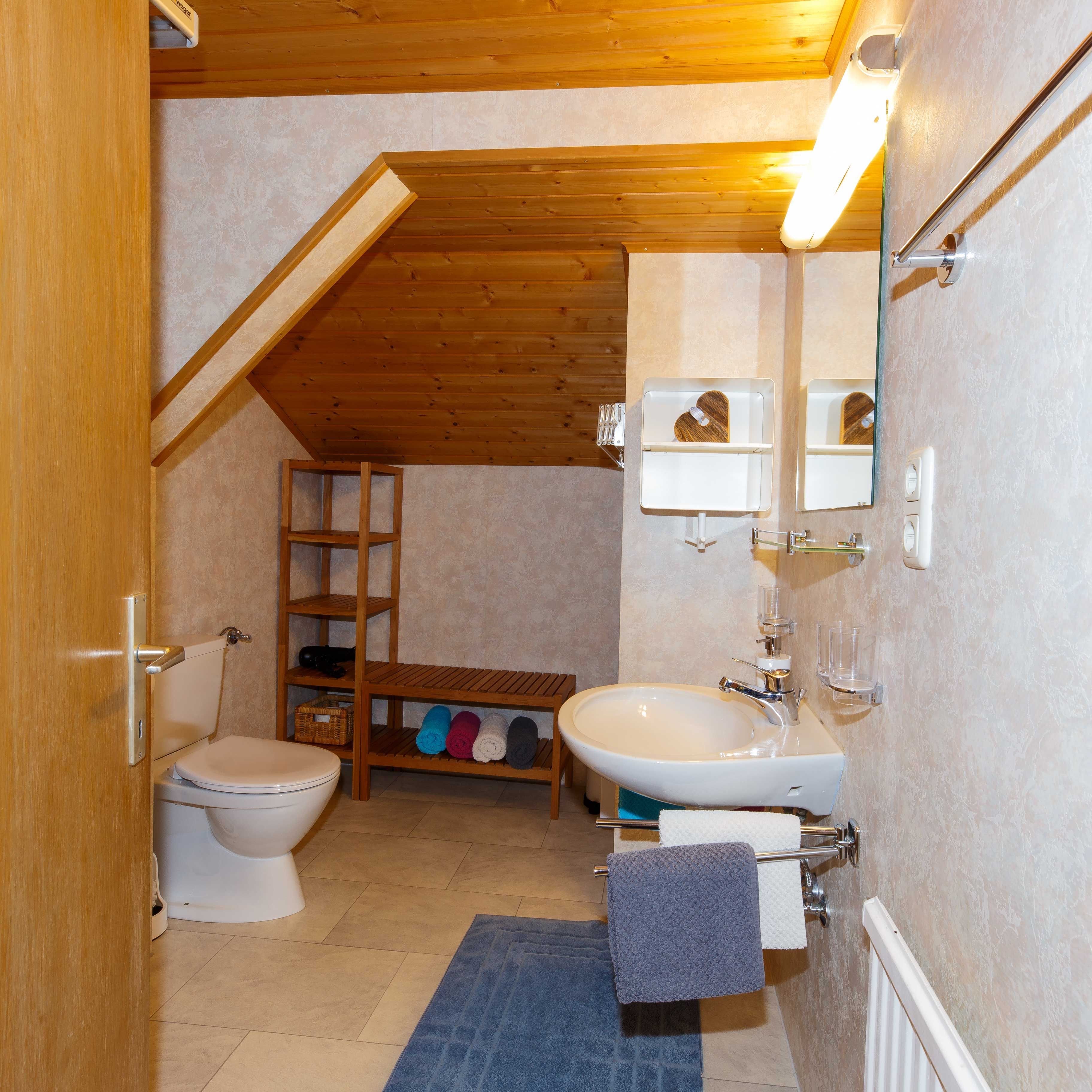 Ein Badezimmer mit Toilette, Waschbecken, Holzregalen und einem Handtuchhalter.
