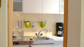 Una cocina con un lavamanos de acero inoxidable, una cafetera y utensilios colgados en un colgador.