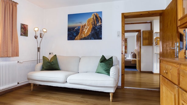 Un salon avec un canapé blanc, un tableau représentant une montagne et un meuble en bois.