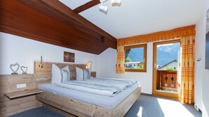 Une chambre à coucher avec un lit en bois, une table de chevet, une tête de lit agrémentée d’un miroir et une fenêtre avec des rideaux.