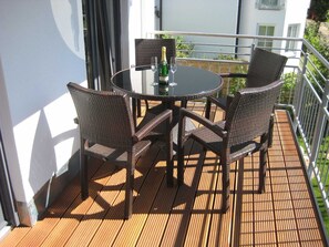 Ein runder Tisch mit vier Korbstühlen auf einer Holzterrasse, eine Champagnerflasche und ein Glas darauf.