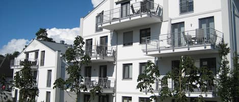 A multi-story residential building with balconies, a clear sky, and surrounding greenery.