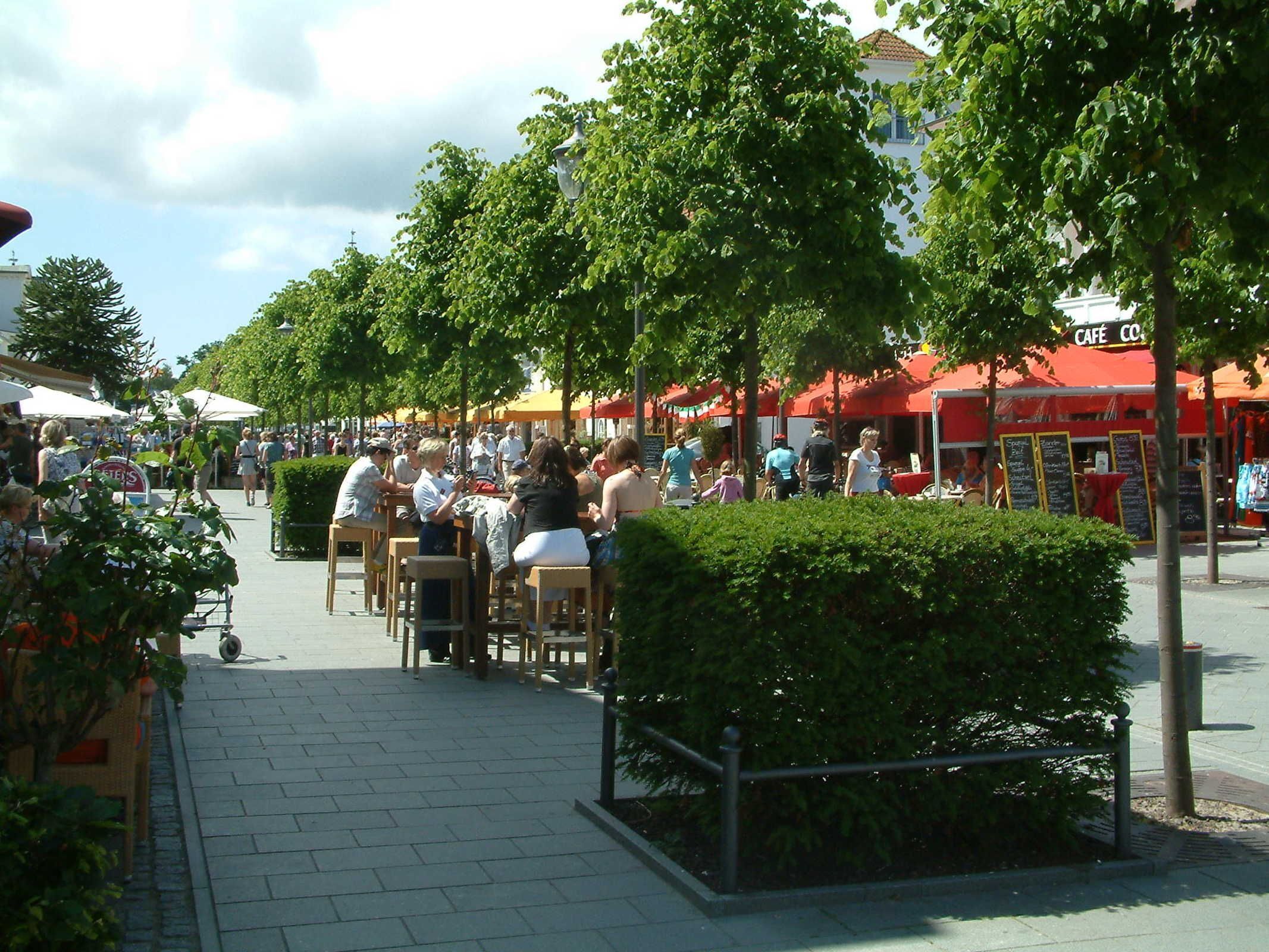 An outdoor café area with tables and chairs, surrounded by trees and a red building with a sign that reads "CAFÉ".