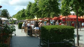 An outdoor café area with tables and chairs, surrounded by trees and a red building with a sign that reads "CAFÉ".