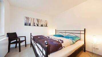 A bedroom with a bed, a chair, a bedside table, and a wall-mounted artwork.
