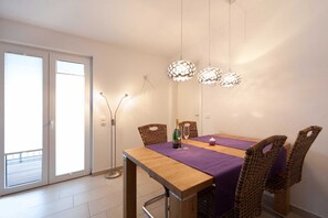 A dining area with a wooden table, purple tablecloth, wicker chairs, pendant lights, and a bottle of champagne.