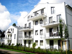 Ein mehrstöckiges Wohngebäude mit Balkonen, einer flachen Dachfläche und blauem Himmel.