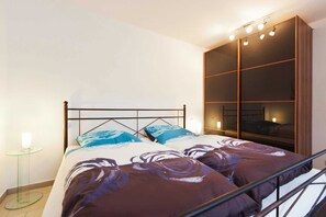 Ein Schlafzimmer mit einem Bett, einem Glastisch, einem Nachttisch und einem großen, beleuchteten Kleiderschrank.