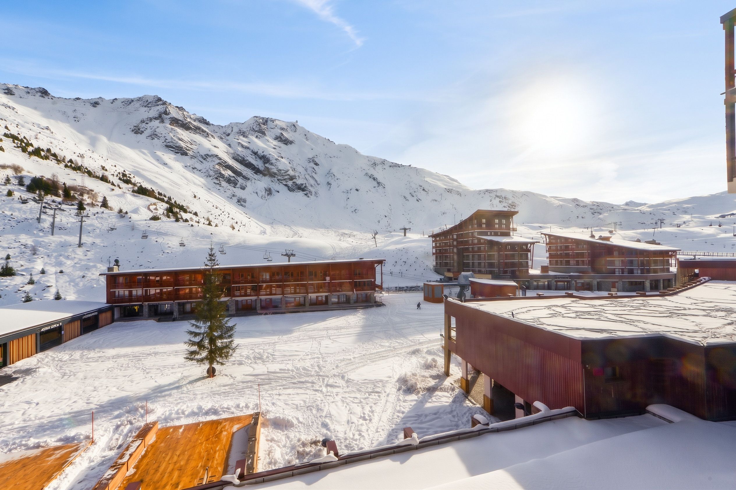 Estación de esquí nevada con edificios modernos, remontes y montañas al fondo.