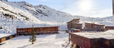 A snow-covered ski resort with modern buildings, ski lifts, and a mountain backdrop.