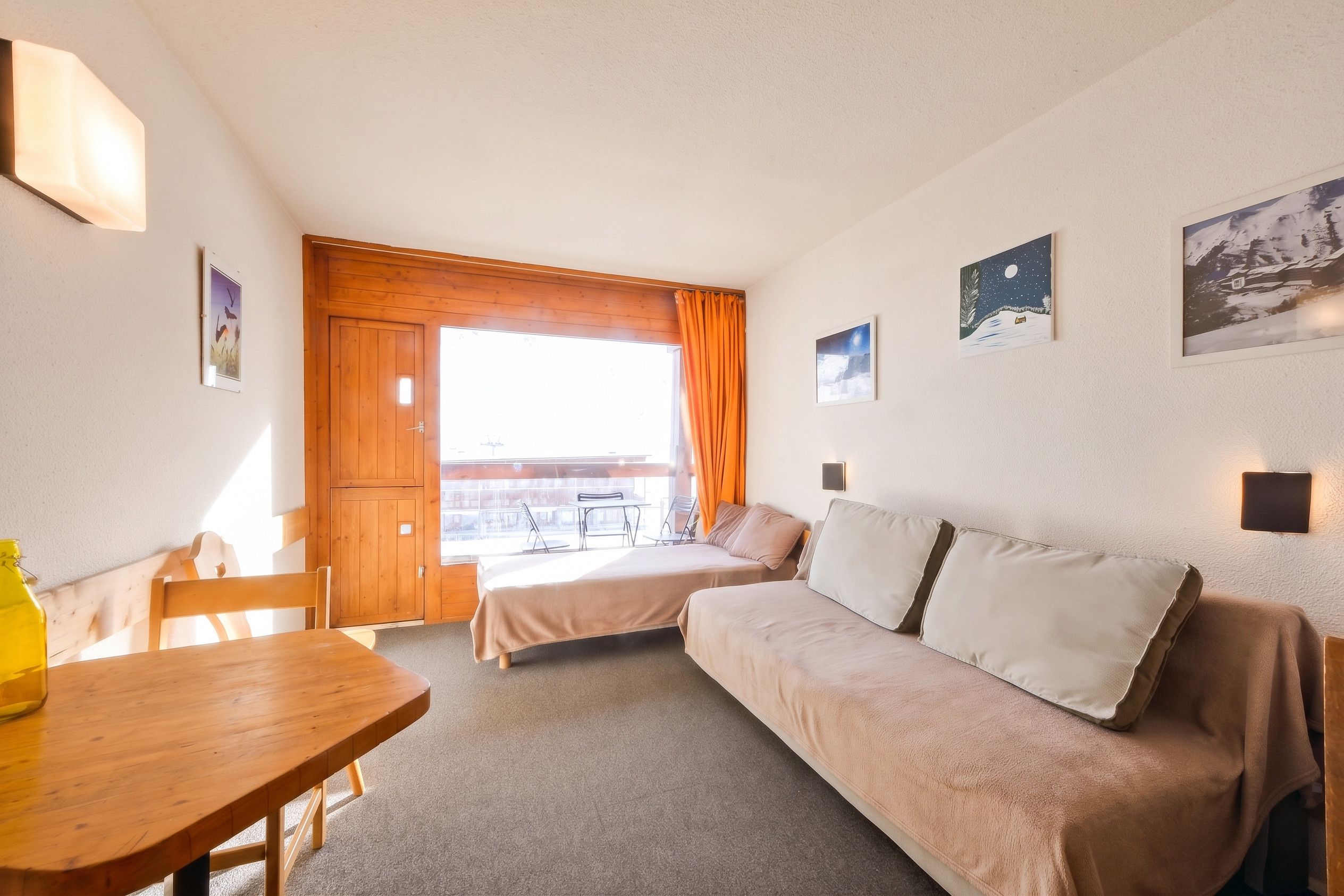 Una habitación con una mesa de madera, dos camas, un sofá y un ventanal con cortinas.