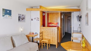 A compact room with a wooden table and chairs, a sofa, and a kitchenette area.