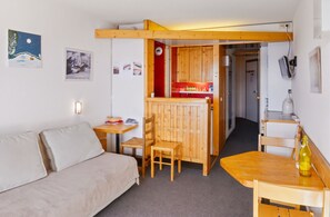 A compact room with a wooden table, a sofa, and a small kitchenette area.
