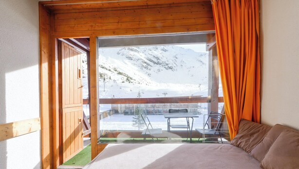 A bedroom with a large window, wooden ceiling, and a view of a snowy mountain.