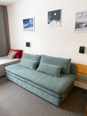 A room with a light blue sofa, a red pillow, and three framed pictures on the wall.