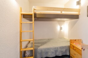 Un lit superposé avec une échelle, une table de chevet et un luminaire fixé au mur, dans une pièce aux murs blancs.