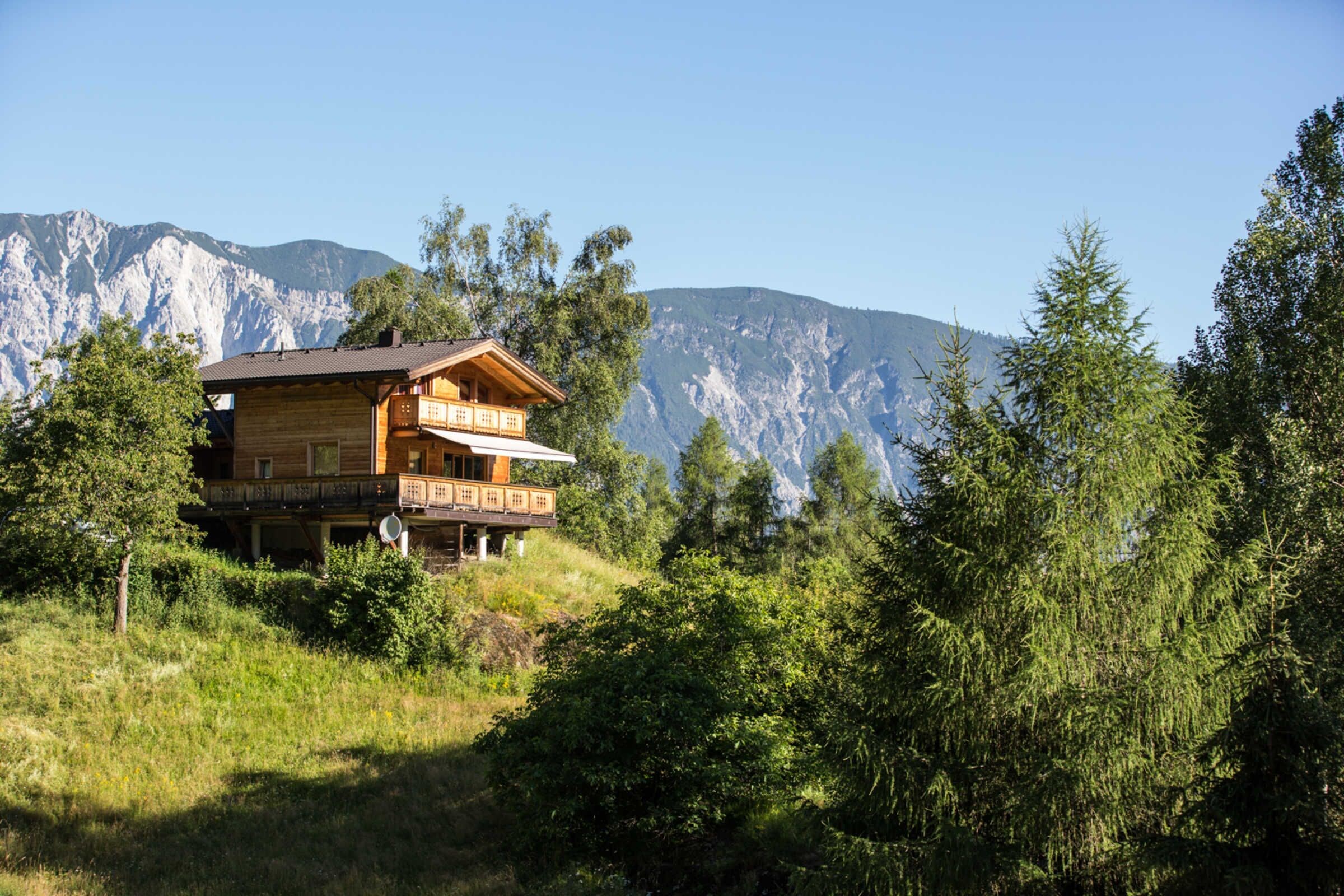 Une cabane en bois dotée d’un balcon, entourée d’arbres et de montagnes.