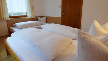 Ein Zimmer mit zwei Betten, einer Holztür und einem Fenster mit Vorhängen.