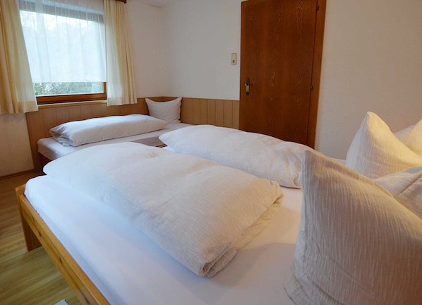 A room with two beds, a wooden door, and a window with curtains.