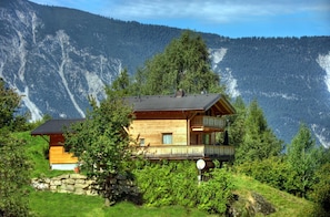 Une cabane en bois dotée d’un balcon, entourée d’une végétation luxuriante et de montagnes.