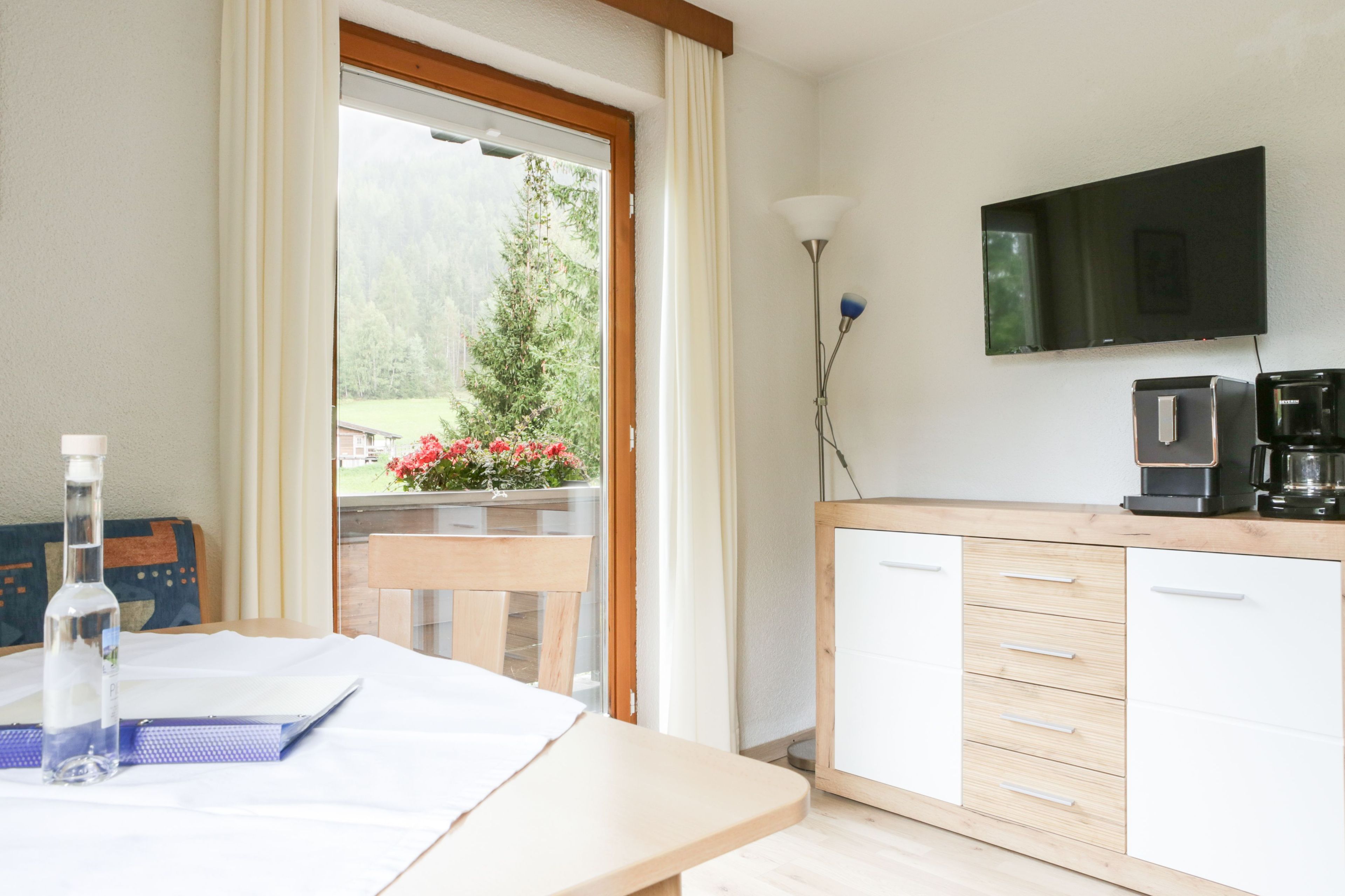 Eine moderne Küche mit Flachbildfernseher, Kaffeemaschine und Blick ins Grüne.