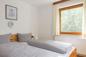 Un dormitorio con dos camas, una ventana con cortinas, un radiador y un cuadro en la pared.
