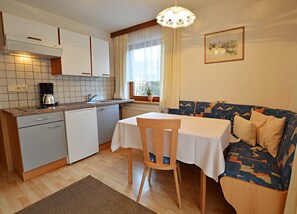 Cocina compacta con comedor, cafetera, radiador y ventana con cortinas.