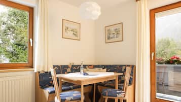 A dining area with a table and chairs, a bench, two framed pictures on the wall, and a window with curtains.