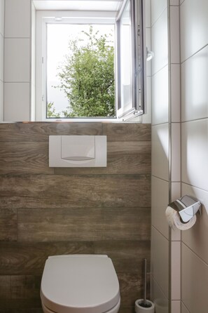 Un baño con un inodoro, una ventana y un dispensador de papel higiénico.