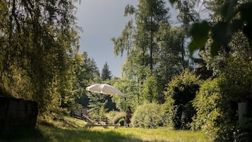 Ein Garten mit einem weißen Sonnenschirm, einer hölzernen Bank und einer Steinmauer.