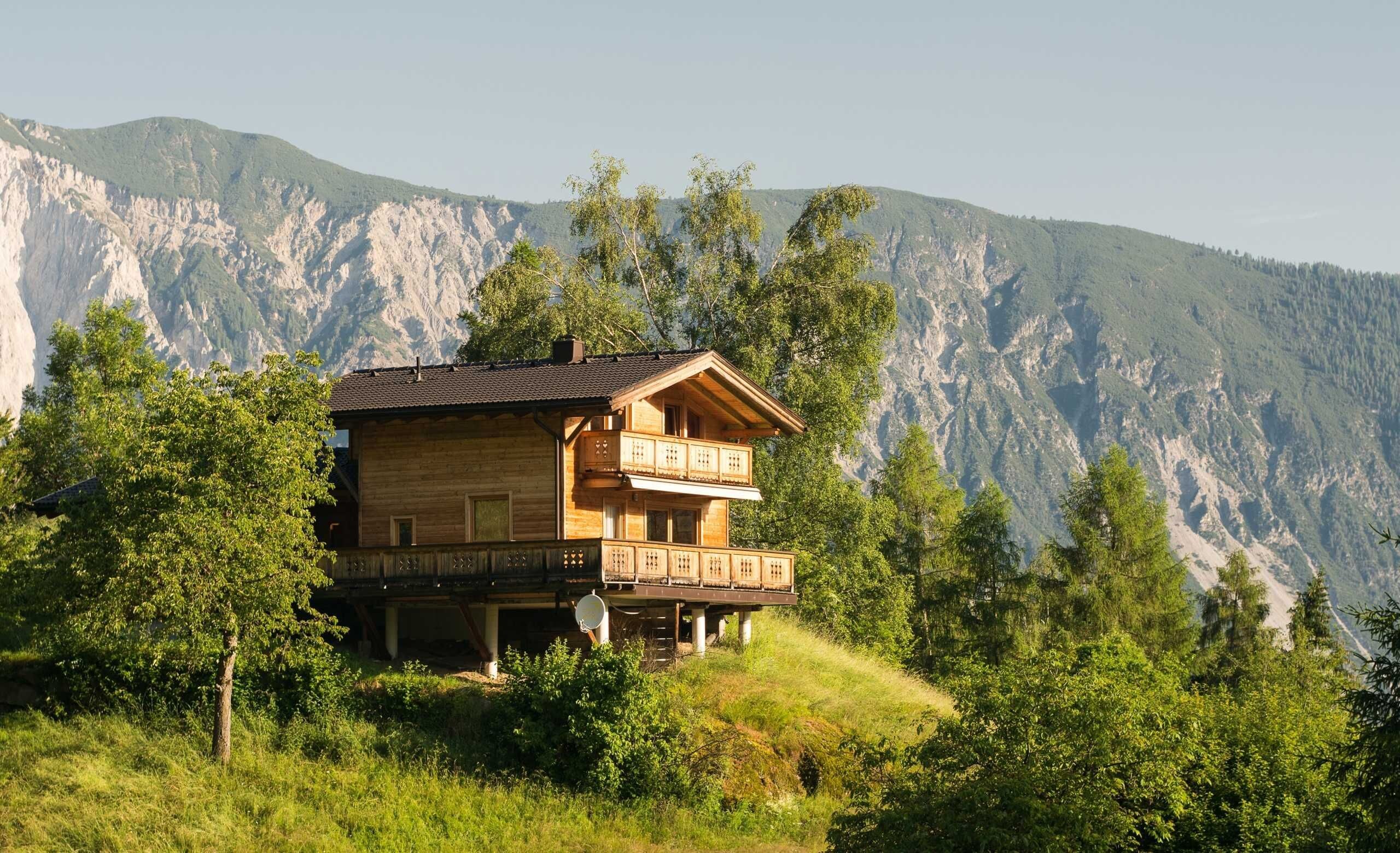 Un chalet de madera de dos pisos con balcones, con montañas al fondo.