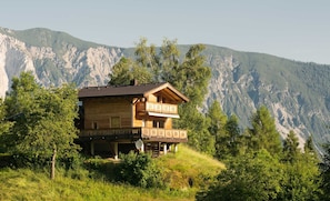 Un chalet de madera de dos pisos con balcones, con montañas al fondo.