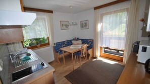 A small kitchenette with a sink and a stove, a dining area with a table and chairs, and a window with curtains.
