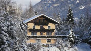 A chalet with a balcony, surrounded by snow-covered trees and mountains.