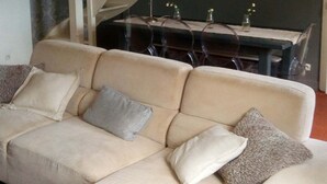 Ein Wohnzimmer mit beiger Couch, einem Esstisch mit Stühlen, einer Treppe und einem Chandelier.