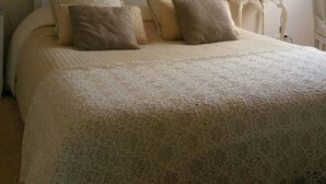 Ein Schlafzimmer mit schrägem Dach, einem Bett mit Spitzenüberwurf und einem Spiegel auf einem Nachttisch.