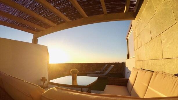 A sunlit outdoor seating area with a round table and cushioned chairs, overlooking a stone wall and a clear sky. - ALTOS DE ARGUINEGUÍN (Mogán Arguineguín)