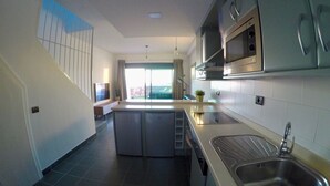 A modern kitchen with a central island, stainless steel appliances, and a large window providing natural light. - ALTOS DE ARGUINEGUÍN (Mogán Arguineguín)