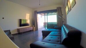 A modern living room with a flat-screen TV, a sofa, and a sliding glass door leading to an outdoor area. - ALTOS DE ARGUINEGUÍN (Mogán Arguineguín)