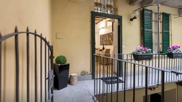 A balcony with a wrought iron railing, a small potted plant, and a flower pot with pink flowers.