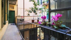 A narrow balcony with a metal railing, potted plants, and a view of a building with balconies and windows.