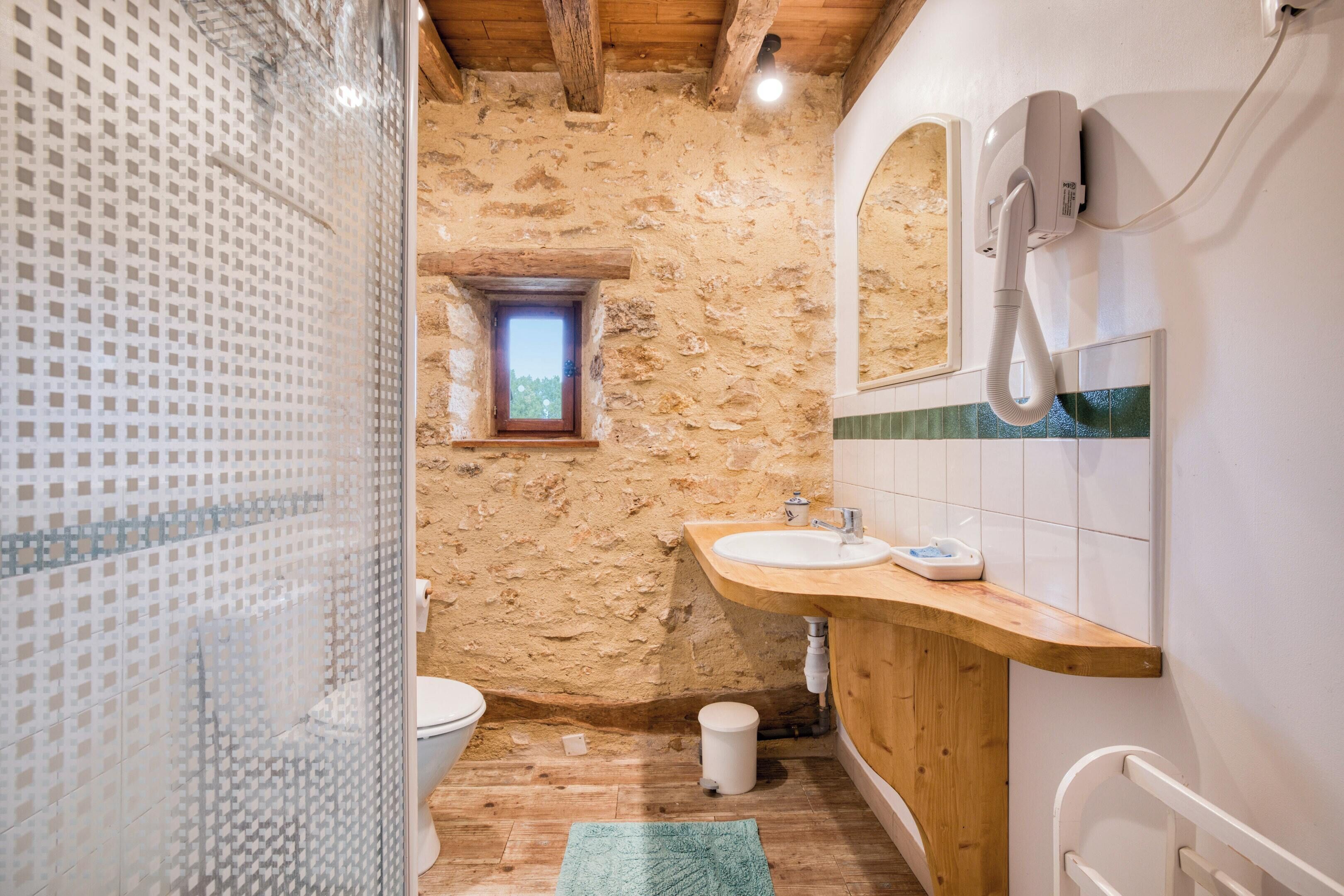Ein Badezimmer mit Steinwand, Holzboden, einer Duschkabine aus Glas, einem Holzbadezimmer-Möbel mit Waschbecken und einem kleinen Fenster.